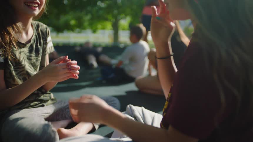 Girls play a hand clapping game sitting on a trampoline in the backyard