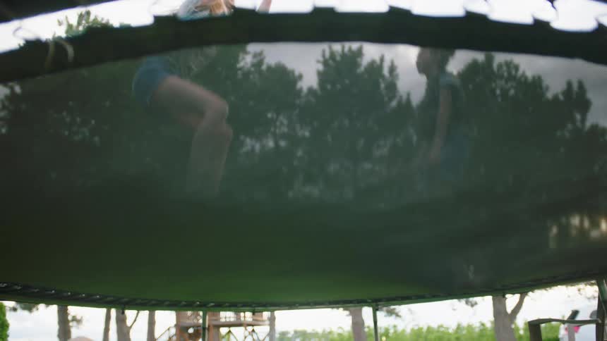 Two kids jump on a trampoline in a backyard