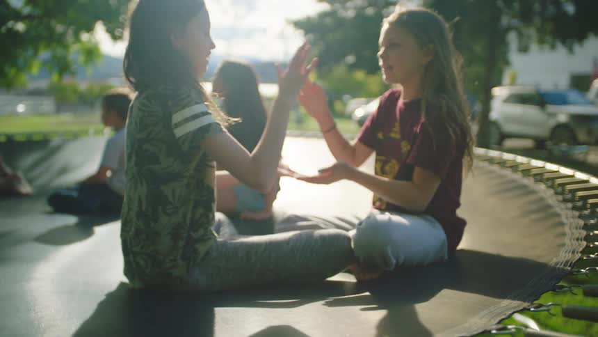 A pair of girls sitting on a trampoline playing clapping games together