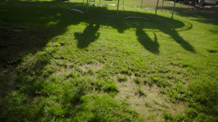 A group of children and teenagers jump around on a trampoline in a yard