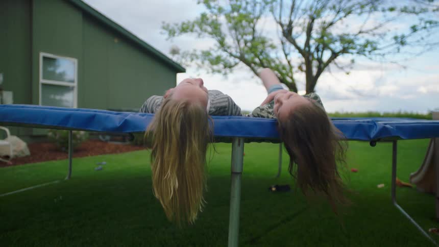 Two young white girls recline on a trampoline in a yard