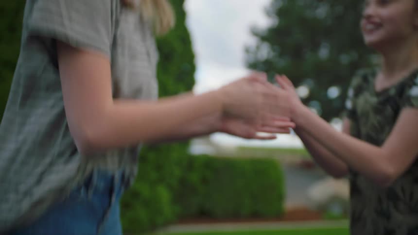 Two girls jump on a trampoline and play hand games