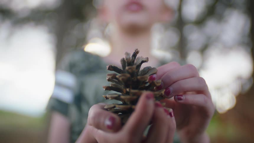 A girl wearing purple nail polish holding a pine cone in front of a camera