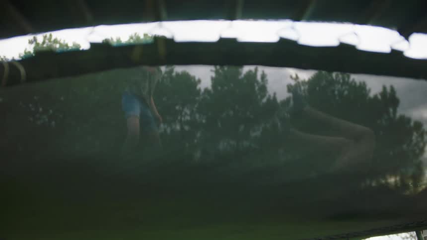 Two girls jump on a trampoline in a yard