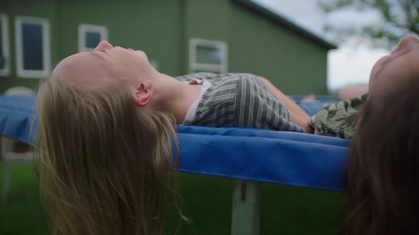 Two girls lie on a trampoline and talk and laugh together