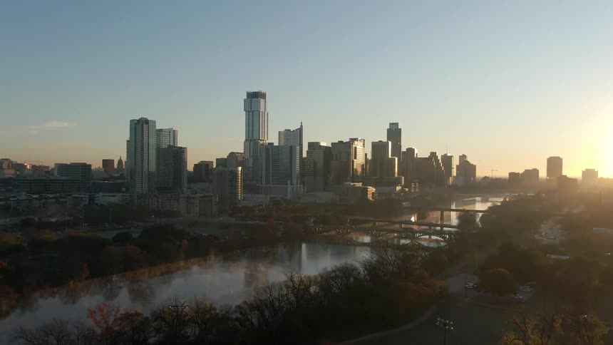 Aerial view of the city with tall buildings next to the river at sunset
