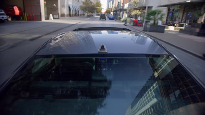 Passenger sits in car driving along downtown city streets past pedestrians