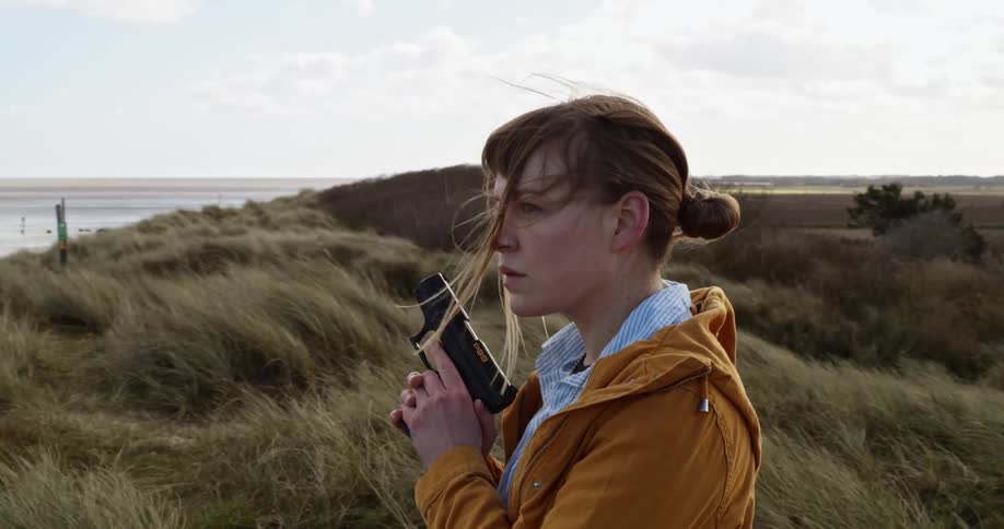A woman holds a handgun while staring into an empty beach