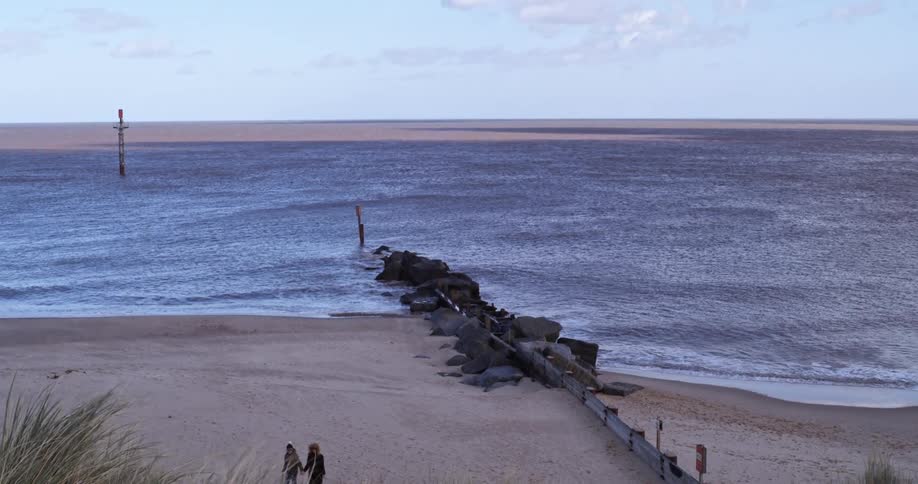 A metal fence separates sections of a beach where two people stand to take a photo