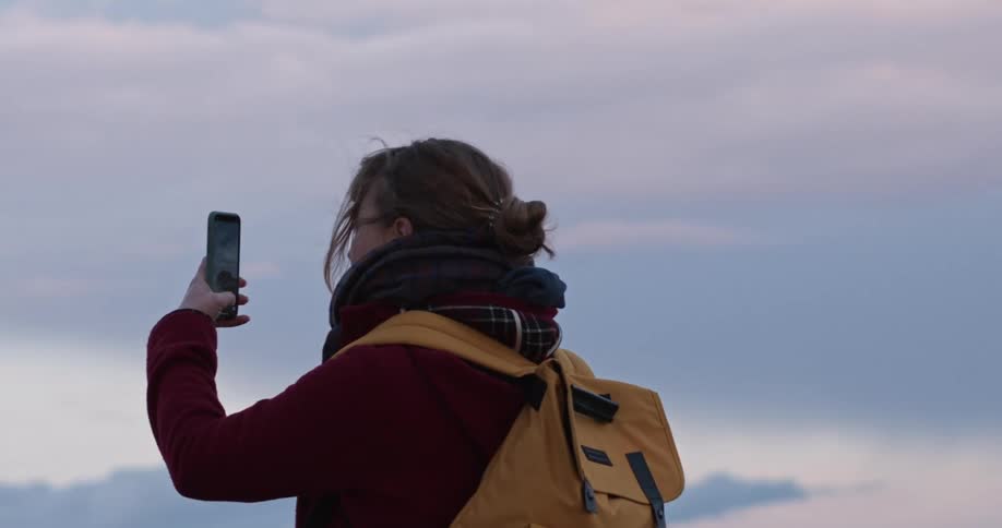 A white woman stands outdoors looking at her smartphone