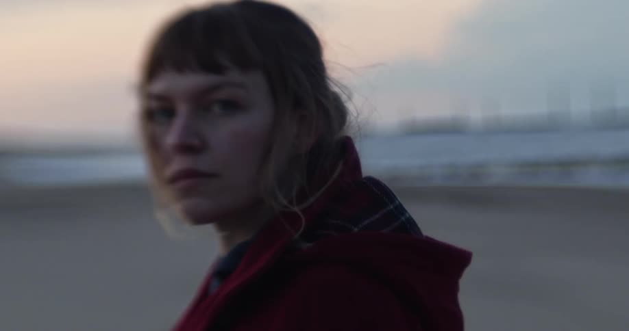 Woman standing on the beach stares at the camera at dusk