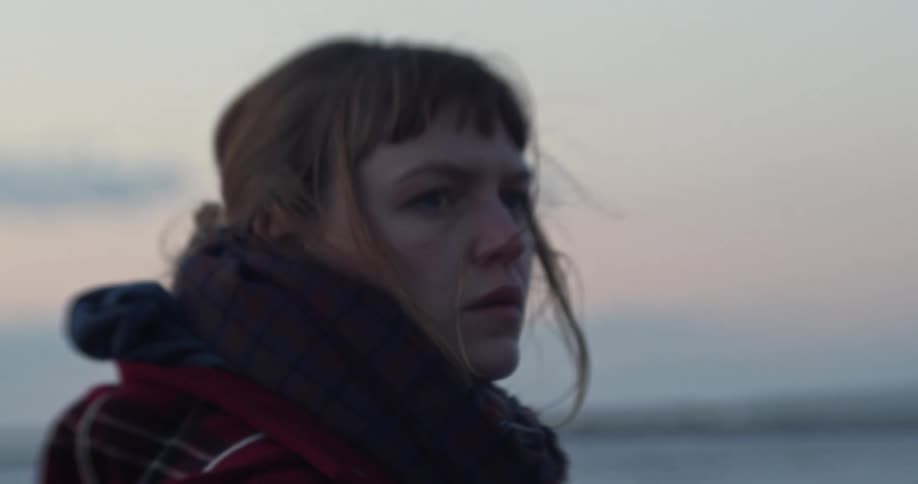 A white woman outdoors turns her head and looks into the distance