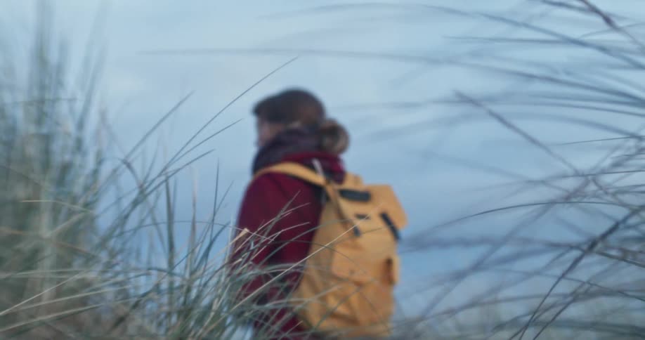 A sad looking white woman stands outdoors with a backpack