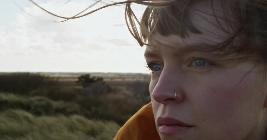 Woman with a nose ring stands in a field while the wind blows her hair