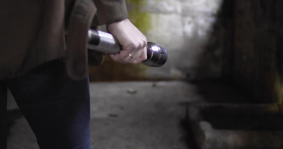 A woman slowly walks forwards carrying and shining a flashlight