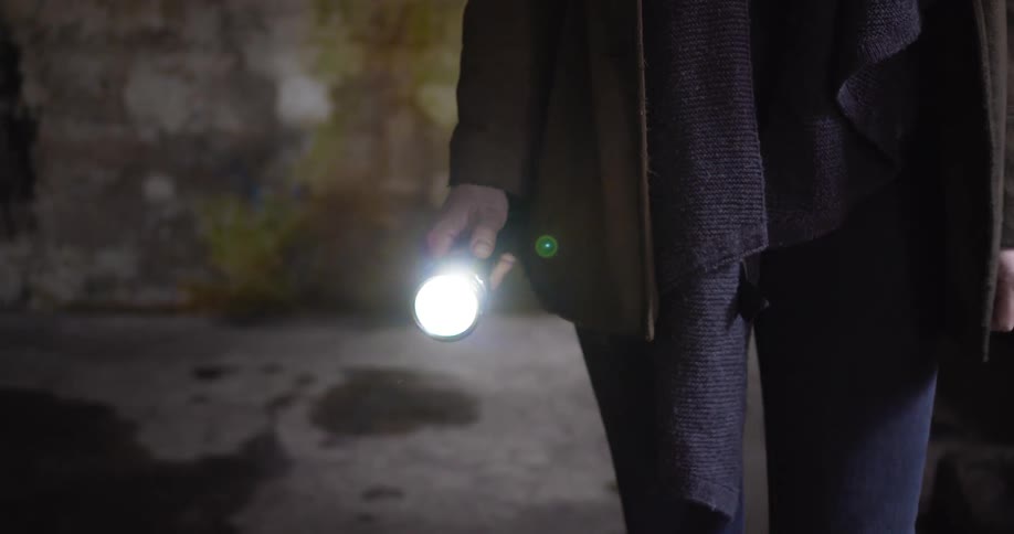 A woman walks in a dark concrete room while holding a flashlight