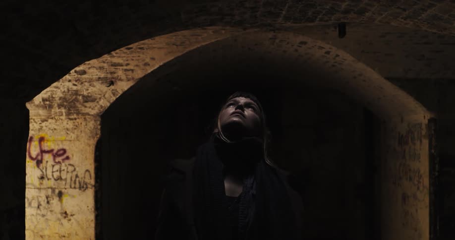 A woman looks up to light in a dark tunnel