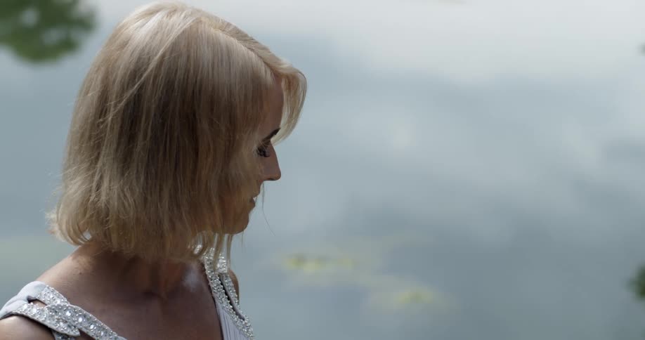 A young blonde woman looks into a calm lake