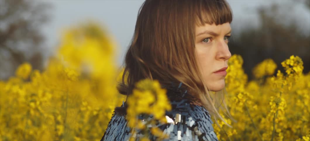 A woman stands in a field of flowers and looks off into the distance