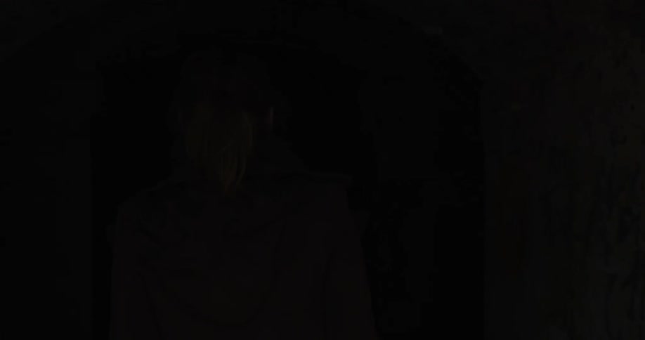 A woman enters a tunnel lined with graffiti while pointing a flashlight ahead