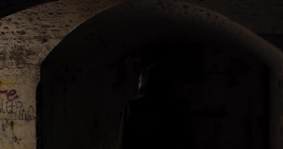 A woman walking down an abandoned tunnel shining a flashlight