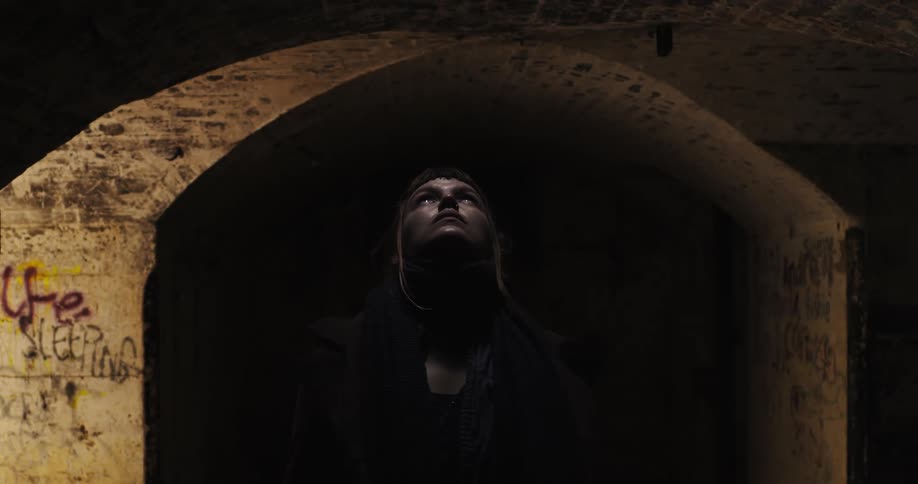A woman walks out of a dark tunnel and looks up into the light