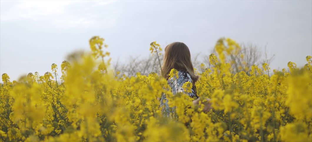 A woman in a sequinned jacket dances through a field of yellow flowers