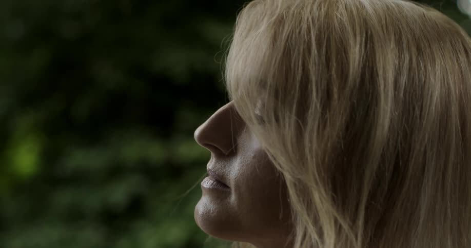 Woman with short blonde hair leans head back with eyes closed outdoors