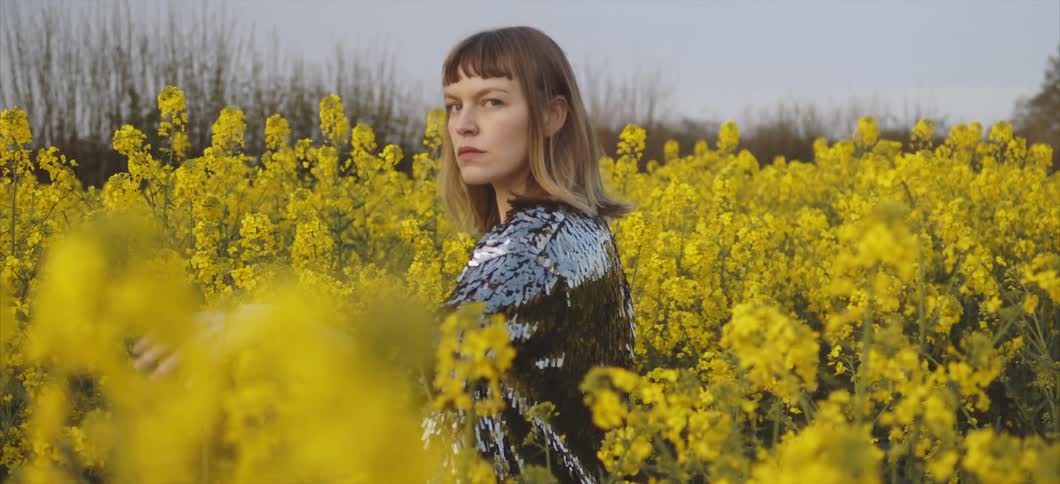 A young woman waves her hand through a field of flowers