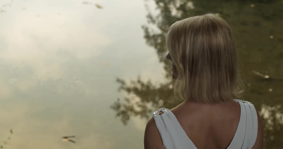 Woman in a white dress stands in front of the calm waters of a lake