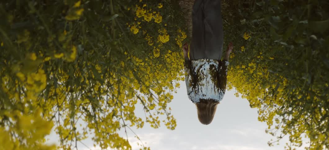 Woman walking on a dirt path through a field of yellow flowers with the camera rotating