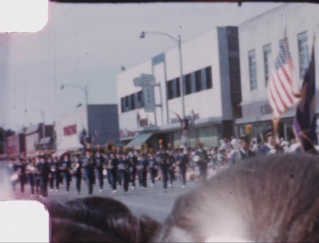 A crowd watches a marching band and honor guard march in a parade
