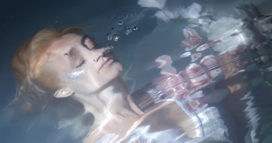 A fully clothed woman holds flowers under the water
