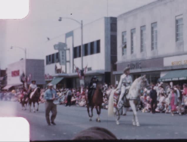 Vintage film of cowboys riding horses on a parade in a small town