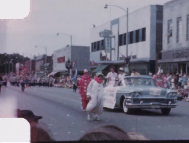 A parade with clowns and marching band on the street of a small town