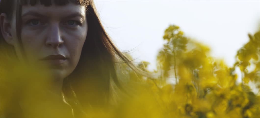 A young woman stands in a field of plants as the wind blows
