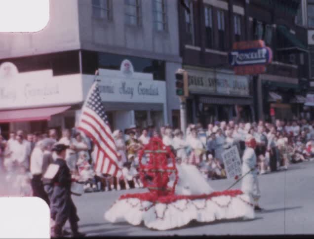 A boy pulls a float and an honor guard marches in a parade through a small town street