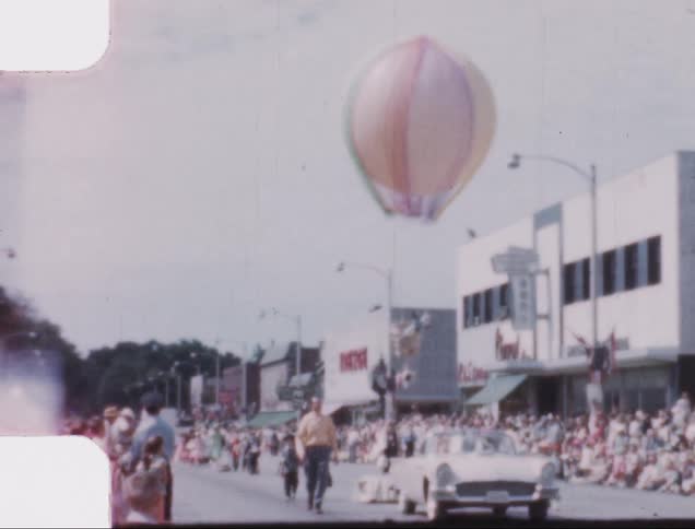 Car leads a parade as a hot air balloon flies overhead