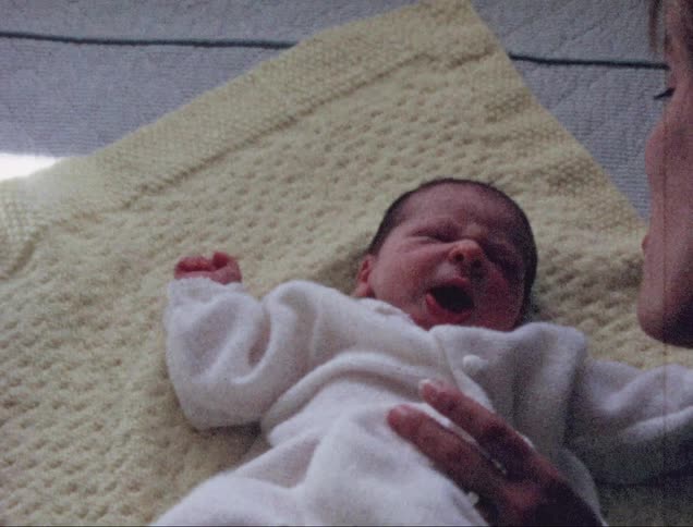 A woman talking to a baby as it lies atop a cloth on a bed