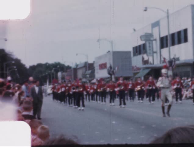 Crowds lining the streets to watch as people in uniform and carrying musical instruments parade through the streets
