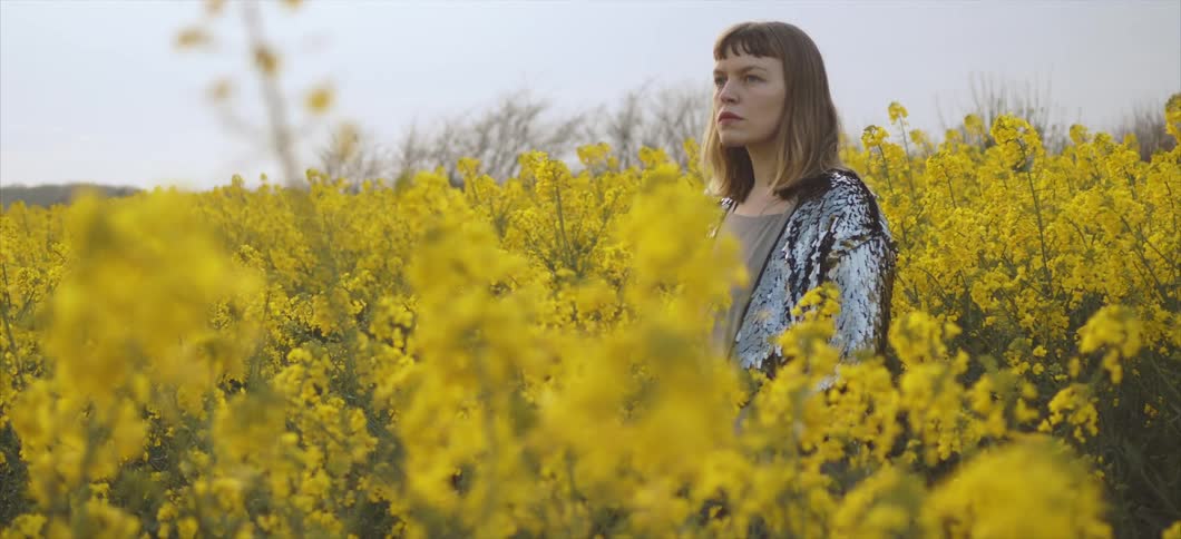 A white woman stands in a field full of yellow flowers