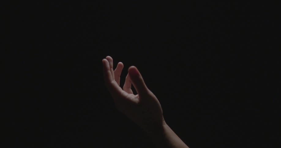 An upturned hand rises up against a black background