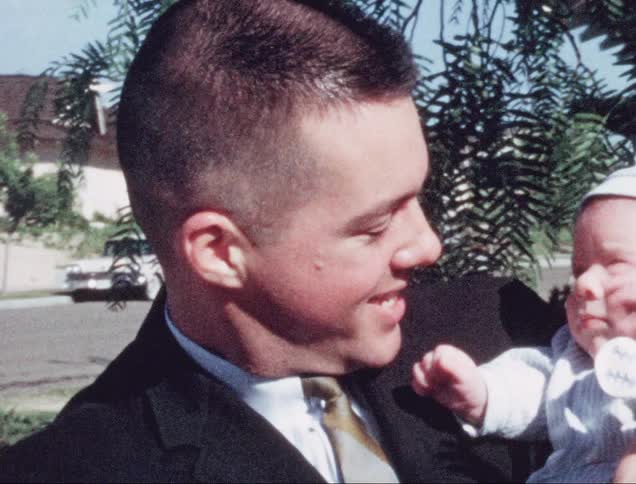 A father holds his infant outdoors next to a street in a neighborhood