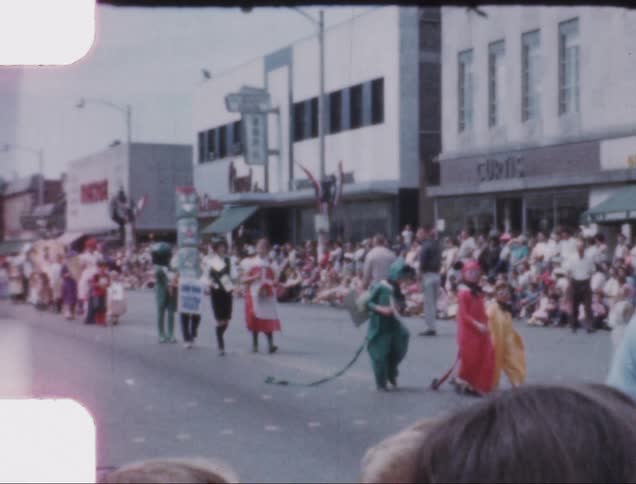 Children in costumes march in a parade down the main street of a small town