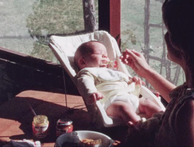 A woman happily feeding a baby with a spoon