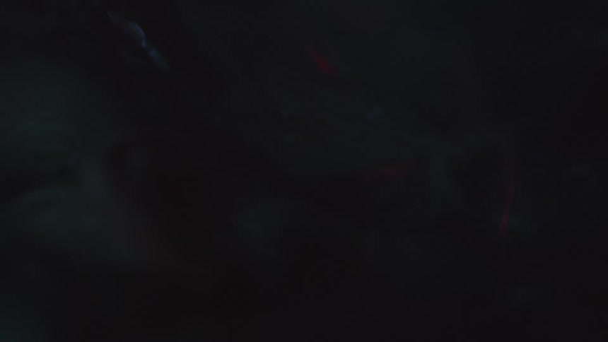 A white person lies outside in the darkness next to a burning flame