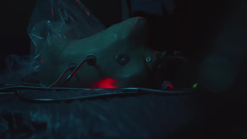 Naked person with cables coming out of its body on a dimly lit room