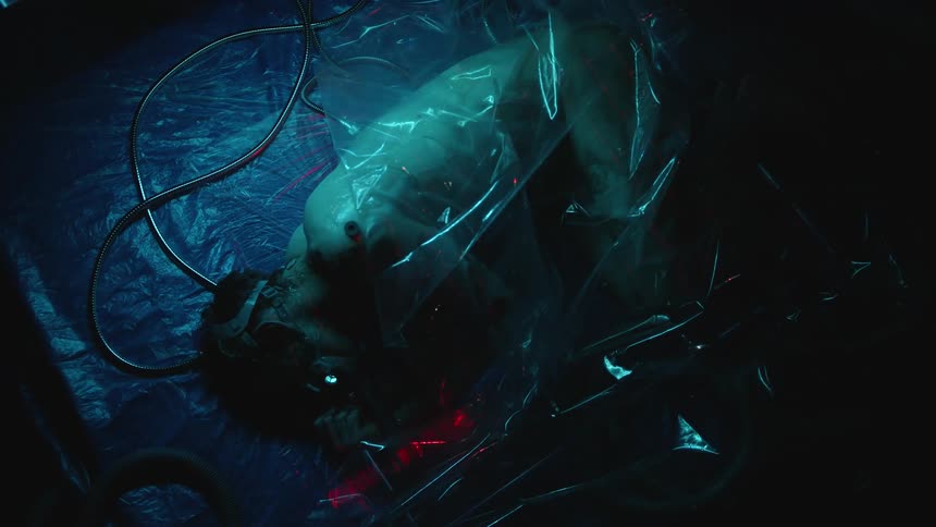 Naked man enclosed in plastic breathes through mask as light brightens and darkens