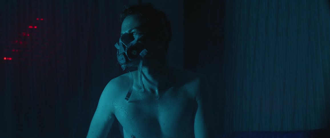 A man sitting down with a mask with a curtain behind him