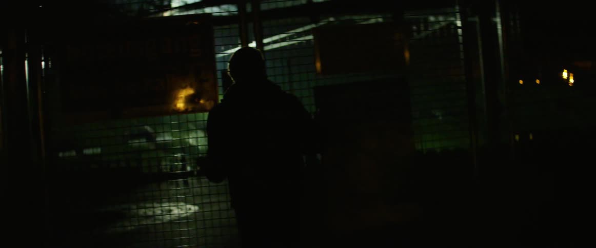 Man walks and holds wire fence at night